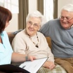 Senior Couple In Discussion With Health Visitor At Home